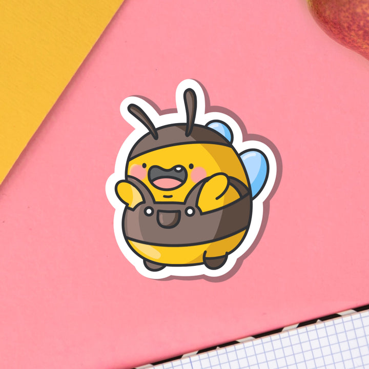 Bumblebee wearing dungarees vinyl sticker on pink table on notebook
