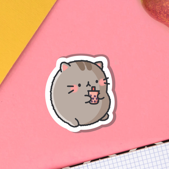Cat drinking bubble tea vinyl sticker on pink table with notebook
