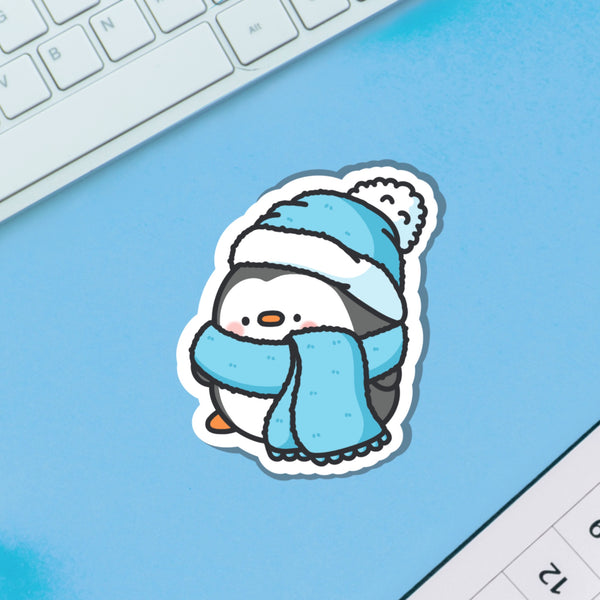 Penguin in scarf and wooly hat vinyl sticker on blue background