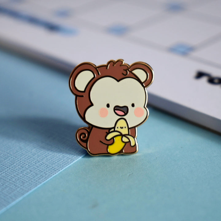 Monkey enamel pin with notepad on blue table