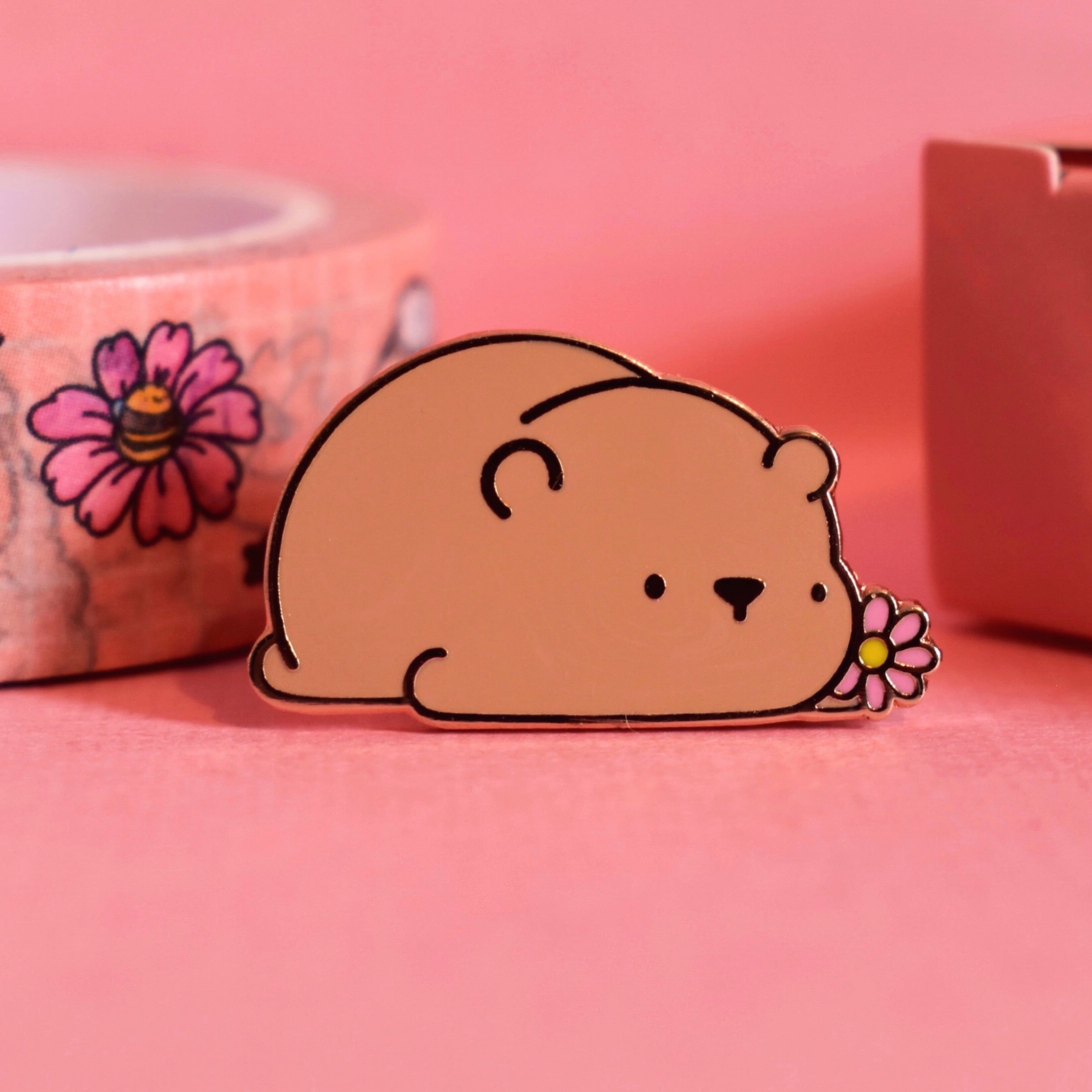 Cute bear enamel pin sat on a pink background